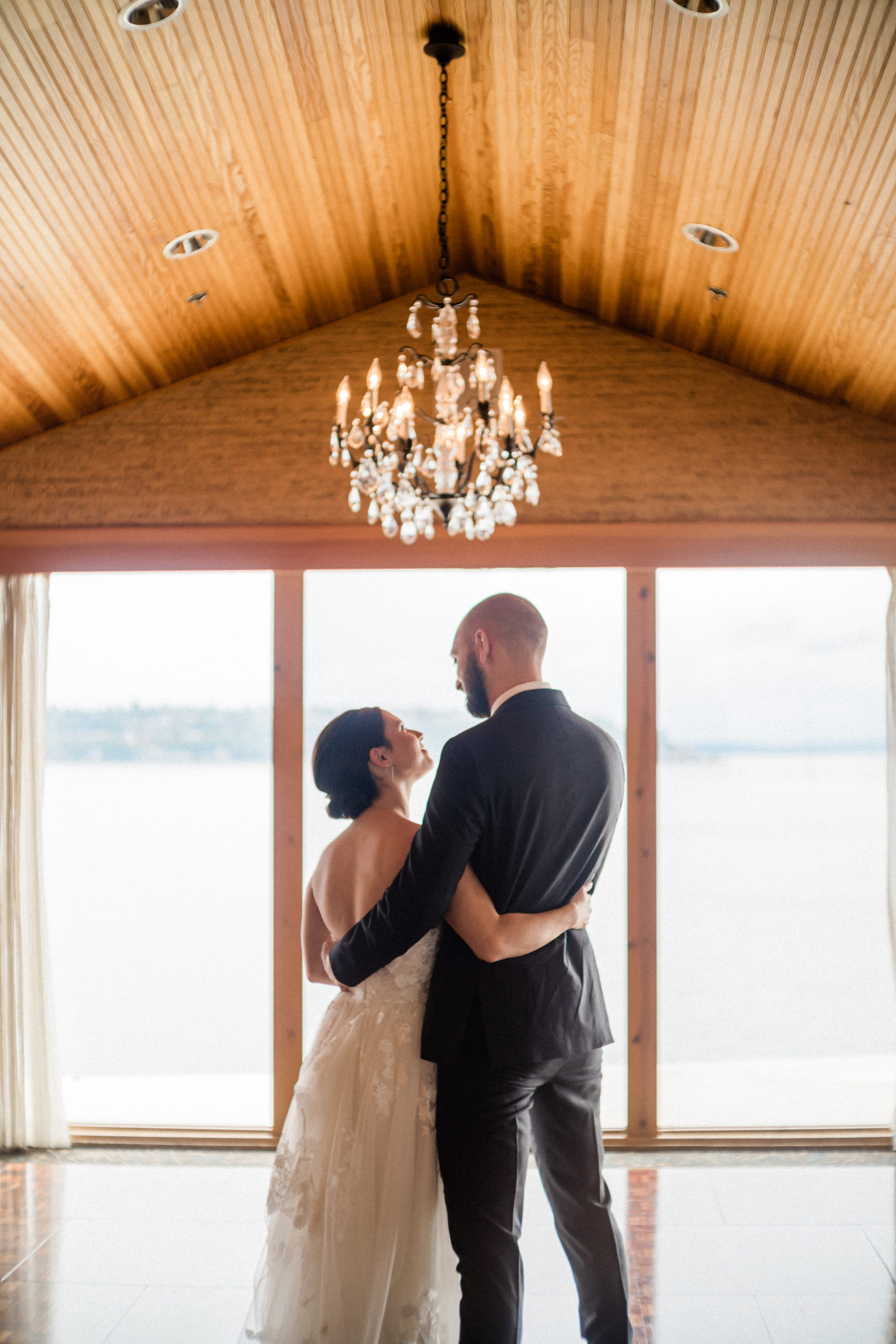 Couple standing in a hotel ballroom with chandelier over their heads.