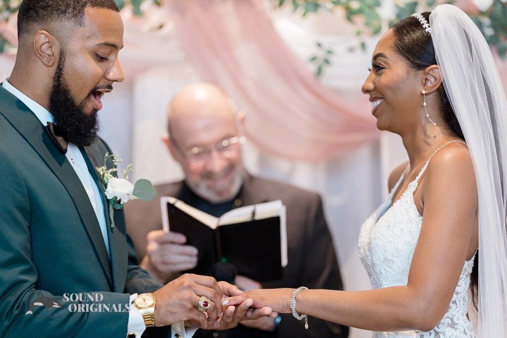 Groom puts on ring on bride&#039;s finger at Briza on the Bay Wedding