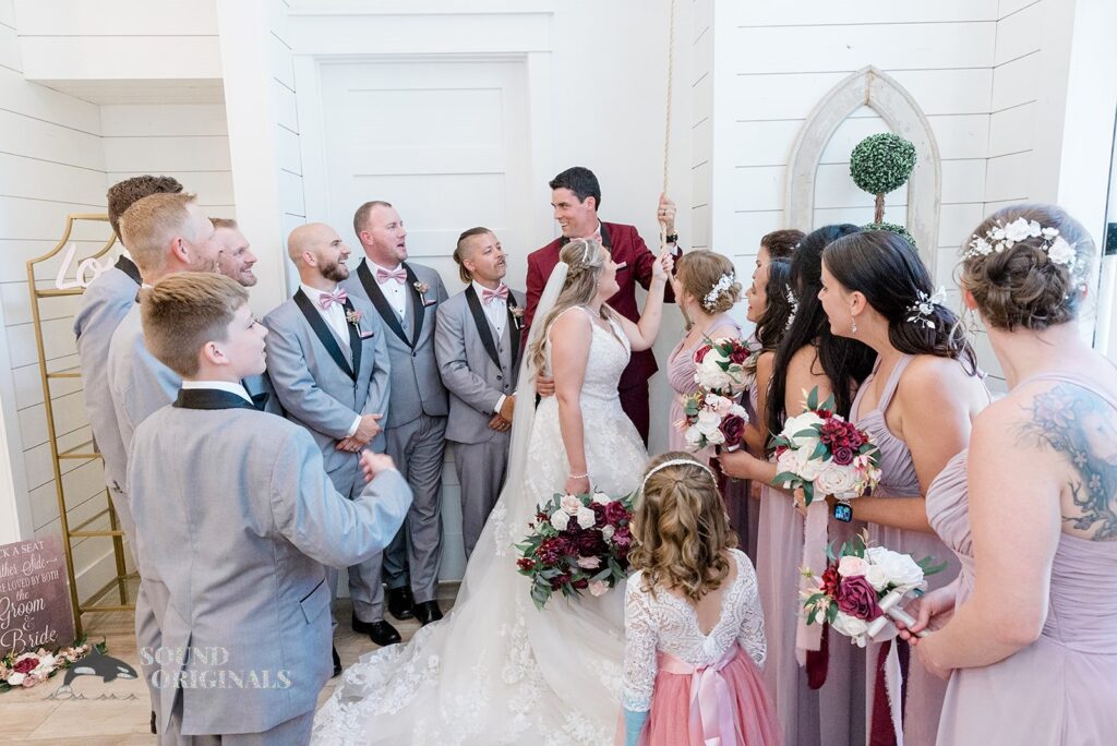 Husband and wife in a happy moment with bridal train and groom&#039;s men after The French Farmhouse Wedding